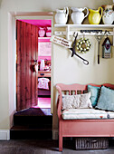 Homeware on shelf above bench seat in hallway of cottage with open pantry door