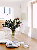 Cut flowers and tableware on wooden dining table
