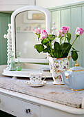 Bemalter Tisch mit Marmorplatte und Kippspiegel mit dekorativem Porzellan und Vase mit rosa Rosen