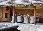 Wicker chairs at table in outdoor room of stone country farm house