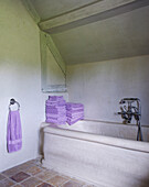 Gefaltete fliederfarbene Handtücher auf einer Badewannenverkleidung in einem Landhaus