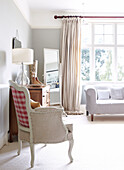 White two seater sofa in sunlit bedroom window with chest of drawers armchair and full-length mirror