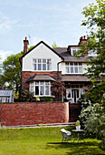 Brick exterior of suburban house with chairs on lawn below patio terrace