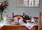 Lit candles with holly arrangement and cut flowers on country table