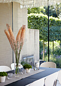Schnittblumen auf einem Esstisch mit Blick durch eine Glaswand auf den Garten