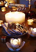 Lit candles and silverware on table with Christmas crackers