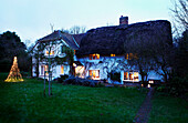 Beleuchtete Weihnachtslichter im Garten eines reetgedeckten Landhauses