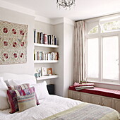 Floral wall hanging above bed with book shelf and window seat in London home UK