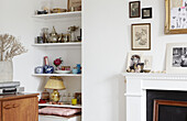 Vintage ornaments on recessed shelving in living room with wooden sideboard and photographic prints on mantle in Hastings home, East Sussex, UK