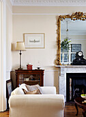 Antique gilt framed mirror on marble fireplace in living room with cream two seater sofa in Warwickshire home, England, UK