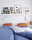 Blau karierte Bettdecke mit orangefarbenen Kissen unter einem Regal mit Kunstwerken im Schlafzimmer eines Hauses in Bussum, Niederlande