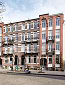 Frau radelt an einem Wohnhaus aus Backstein in Amsterdam, Niederlande, vorbei