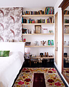 Geblümter Bodenteppich und Bücherregale mit Schuhablage im Schlafzimmer einer modernen Wohnung, Amsterdam, Niederlande
