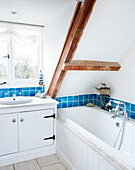 White attic bathroom with ceiling beam and blue tiled splashback in Nottinghamshire barn conversion England UK
