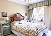 Embroidered bed cover in bedroom with curtain pelmet above window in traditional country house Welsh borders UK