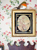 Robin on gilt framed artwork with floral wallpaper in Oxfordshire country house England UK