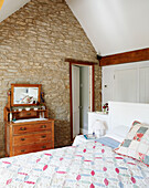 Wooden chest of drawers with mirror in exposed stone attic bedroom of rural Oxfordshire cottage England UK