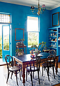 Vintage wooden table and chairs in bright blue dining room with open back door in Auckland home North Island New Zealand