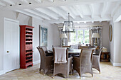 Wicker chairs at circular table with red painted wine rack in Buckinghamshire dining room UK