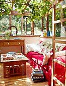 Rotes Sofa im sonnenbeschienenen Wintergarten eines Cottage in Devonshire UK