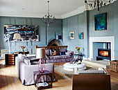 Beleuchtetes Feuer und moderne Kunstwerke mit fliederfarbenen Sofas im getäfelten Wohnzimmer eines Herrenhauses in Northumbria England UK