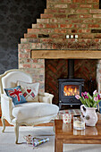 White upholstered armchair at lit fireside in County Durham cottage, England, UK
