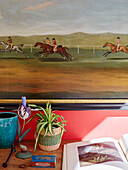 horseracing artwork above book and cactus on console in 18th century Northumbrian mill house, UK