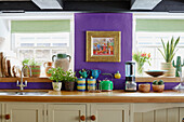 Roman blinds at sunlit windows in purple kitchen of 18th century Northumbrian mill house, UK