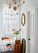 Cut flowers on drawers with binoculars on folding chair at window with lace curtain in Country Durham home, North East England