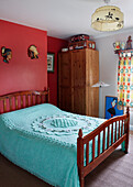 Türkisfarbene Bettdecke auf Holzbett mit roter Wand in einem Haus in der Grafschaft Durham, Nordostengland, UK