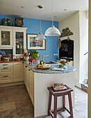 Book and stool with fruit on breakfast bar and glass pendant lights in blue kitchen of 19th century Georgian townhouse in Talgarth, Mid Wales, UK