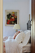 Framed still life above double bed with lace and embroidered cushions in Yorkshire home, England, UK