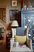 Armchair and lamp with handpainted cupboard in Chippenham home, Wiltshire, UK