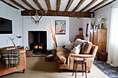 Brown leather sofa and chair with lit woodburner in beamed Warwickshire farmhouse, England, UK