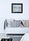 Assorted cushions on white bench seat below artwork in Edwardian London flat, UK