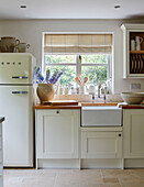 Crockery and utensils on kitchen sink at window with upright fridge in West Sussex barn conversion, UK