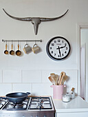 Metal antlers and clock above kitchenware with pan on gas hob in Tunbridge Wells home, Kent, UK