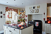 Blumen auf einer Kücheninsel mit Herzdekoration und Girlande in einer weihnachtlichen weißen Einbauküche in einem britischen Haus