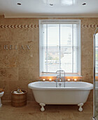 Freestanding candlelit rolltop bath at window with Venetian blinds and single word ' RELAX' in, UK home