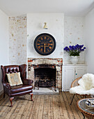 Leather armchair at fireside with large clock in Camber cottage, East Sussex, UK