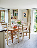 Cut flowers and sponge cake on wooden table with chairs in Sandford St Martin cottage, Oxfordshire, UK