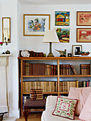 Hardbacked books on shelves with framed art in Oxfordshire farmhouse, UK
