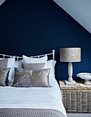 Blue and gold attic bedroom with woven side table in North Yorkshire home, UK