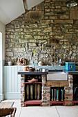 Wellington boots and sink with exposed stone wall in entrance room of Northumberland farmhouse, UK