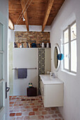 White wahstand at window with exposed stone wall and shelf in Brittany cottage, France