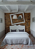 Double bed with exposed stone wall empty picture frame and lamps in Brittany cottage, France