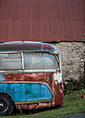Old blue bus outside stone barn with corrugated metal roof in Radnorshire-Herefordshire border
