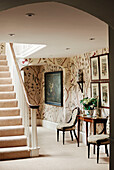 Floral wallpaper and chairs with console in hallway of Cotswolds home, UK