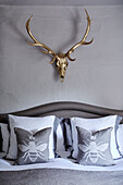 Gold antlers above grey bed with bee pillows in Devon home, UK