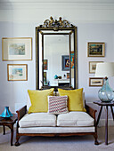 Gilt framed mirror above two seater sofa with yellow velvet curtains in Northern home, UK